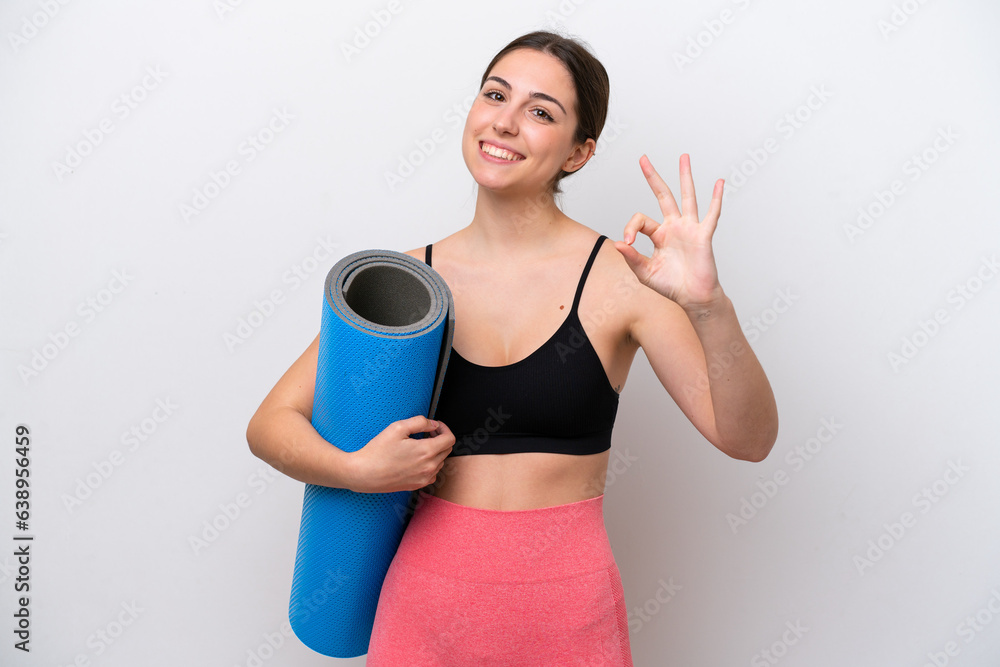 Young sport girl going to yoga classes while holding a mat isolated on white background showing ok sign with fingers Young sport girl going to yoga classes while holding a mat isolated on white background showing ok sign with fingers