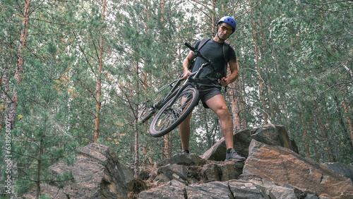 mountain bike.A man wearing a helmet and sportswear carries a bicycle through a rocky terrain.An active lifestyle.Bicycle in hand