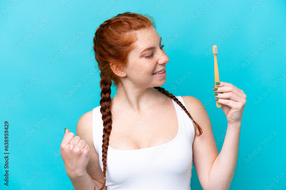 Obraz premium Young caucasian reddish woman brushing teeth isolated on blue background celebrating a victory