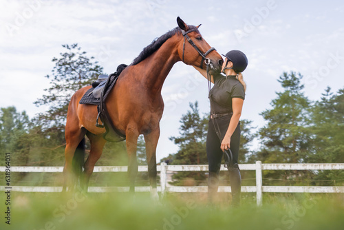 Young female jockey in helmet petting her horse in countryside