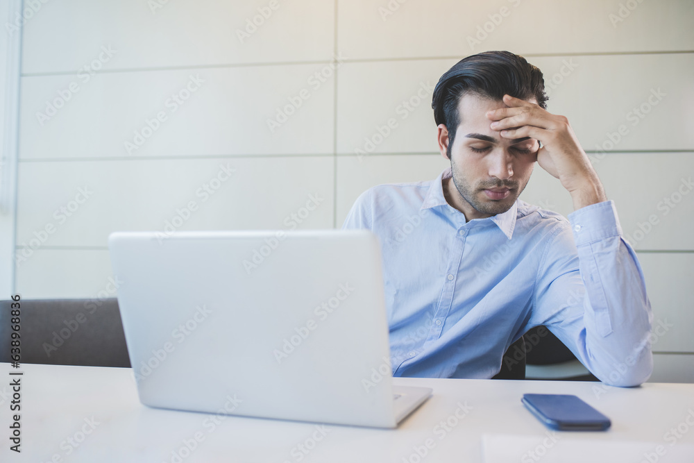 Young indian businessman indoors office working suffering headache Young indian businessman indoors office working suffering headache