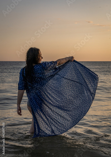 kobieta stojąca w morzu z uniesiona sukienką