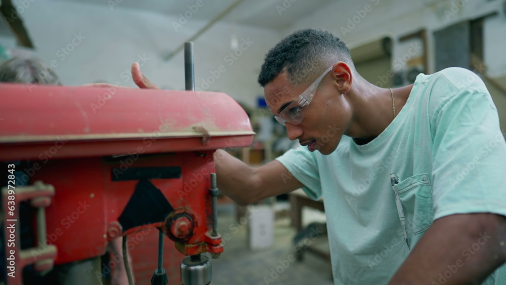 One happy young black carpentry apprentice using industrial machine, turns toward camera smiling. Friendly portrait of a worker engaged with job occupation One happy young black carpentry apprentice using industrial machine, turns toward camera smiling. Friendly portrait of a worker engaged with job occupation