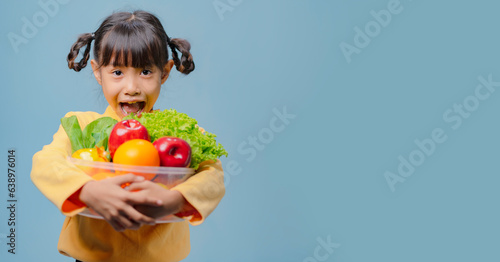A little girl is holding a bowl of fruits and vegetables.