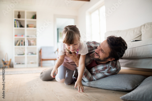 Young caucasian father and daughter hugging and playing together in the living room at home