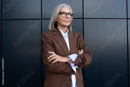 confident well-groomed old lady with gray hair in glasses is dressed in a brown jacket and shirt spends lunchtime walking along the street