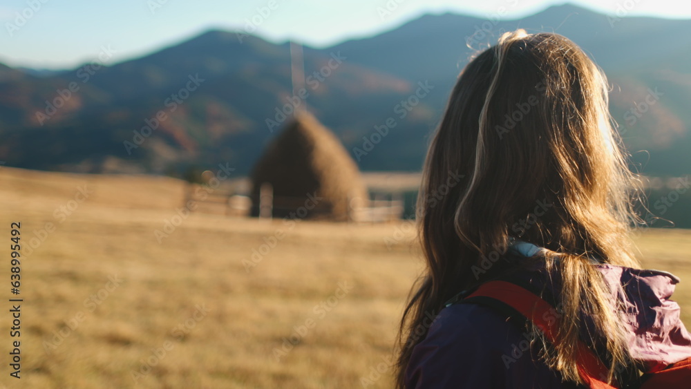 Tourist woman enjoy autumn sunset landscape in Carpathian mountains, Ukraine. Long hair caucasian girl looking on yellow grass field, village countryside. Travel, hiking, freedom and active lifestyle