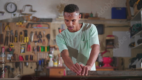 Young apprentice at carpenter workship sawing and measuring piece of wood with industrial equipment. People at craftmanship work, job occupation concept