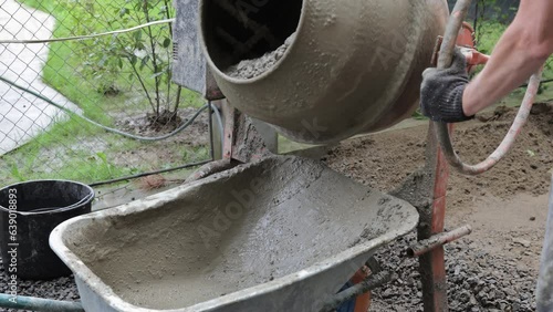 A concrete mixer pours cement mortar into a wheelbarrow. A close-up image of an electric concrete mixer pouring ready-made cement mortar into a wheelbarrow