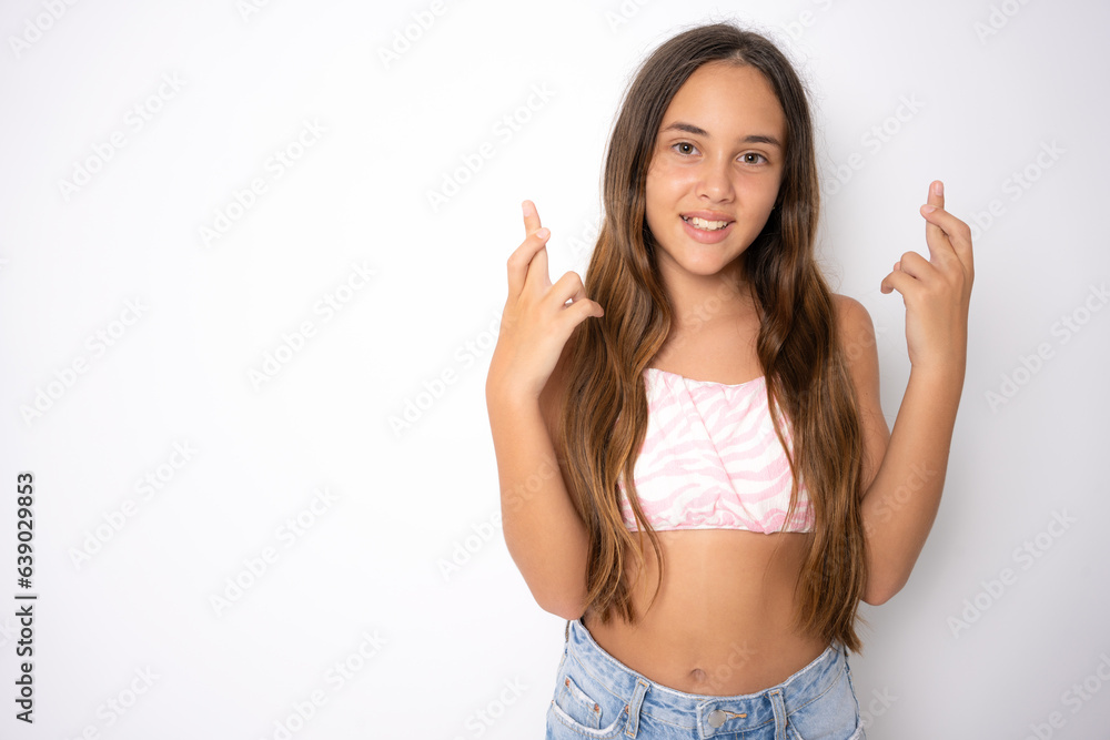 Teenager child holding fingers crossed for good luck. Portrait of cheerful girl prays and hopes dreams come true, crosses fingers for good luck, isolated on white studio background. Teenager child holding fingers crossed for good luck. Portrait of cheerful girl prays and hopes dreams come true, crosses fingers for good luck, isolated on white studio background.