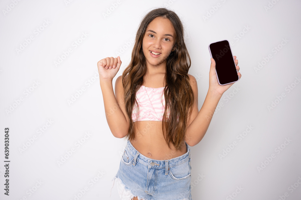 Naklejka premium Closeup photo of young cute schoolkid girl wearing summer clothing celebrate good mood eshopping hold black touchscreen phone isolated on white background