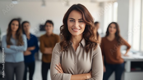 Successful businesswoman standing in creative office and looking at camera while smiling. Portrait of beautiful business woman standing in front of business team at modern agency with copy space