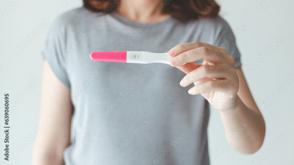 A woman holding a pregnancy test and discovering her positive result. - obrazy, fototapety, plakaty 