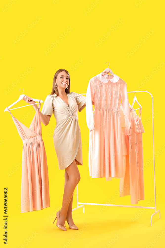 Beautiful happy young woman and rack with different stylish clothes on yellow background Beautiful happy young woman and rack with different stylish clothes on yellow background
