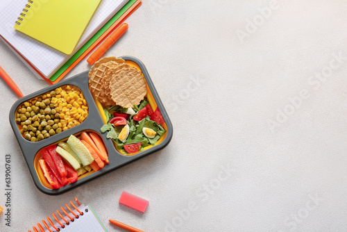 Lunchbox with delicious food and different stationery on light background