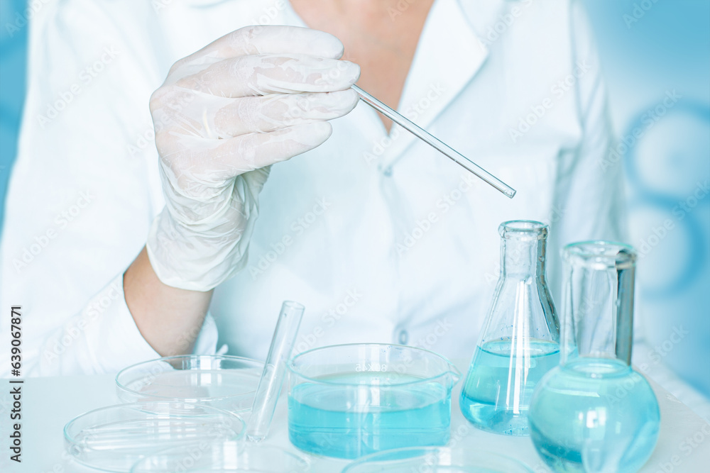 In the lab: Assistant manipulates materials. Wearing gloves and white attire. Utilizing glassware. Transparent blue liquid used. In the lab: Assistant manipulates materials. Wearing gloves and white attire. Utilizing glassware. Transparent blue liquid used.