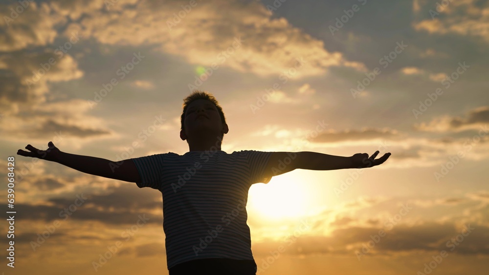 Happy family, Child raised his hands to sky in park at sunset, true faith. Little boy prays against background of sky and sun. Religion and god, childhood dreams. Child boy plays in park against sky