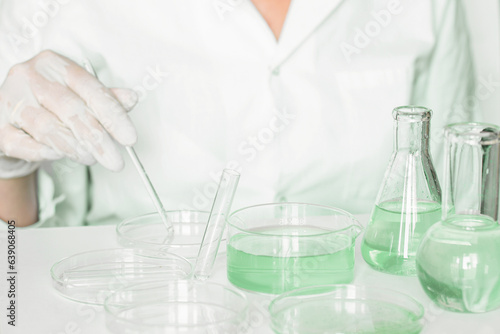 Lab stage: Lab assistant meticulously engages in manipulations within the laboratory. Donning lab coat. Green colors prominent. Using glass apparatus. 
