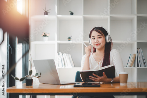 Portrait of a cheerful young woman listening to music with headphones and using laptop computer while leaning on a couch at home