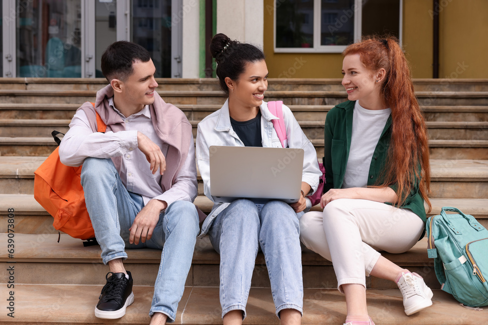 Happy young students studying together with laptop on steps outdoors