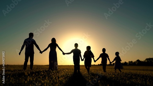 Parents  happy children go to sun. People walk in nature. Big family holding hands walk in park at sunset. Dad mom  son  daughter walk  walk together outdoors. Concept of happy family childhood dream