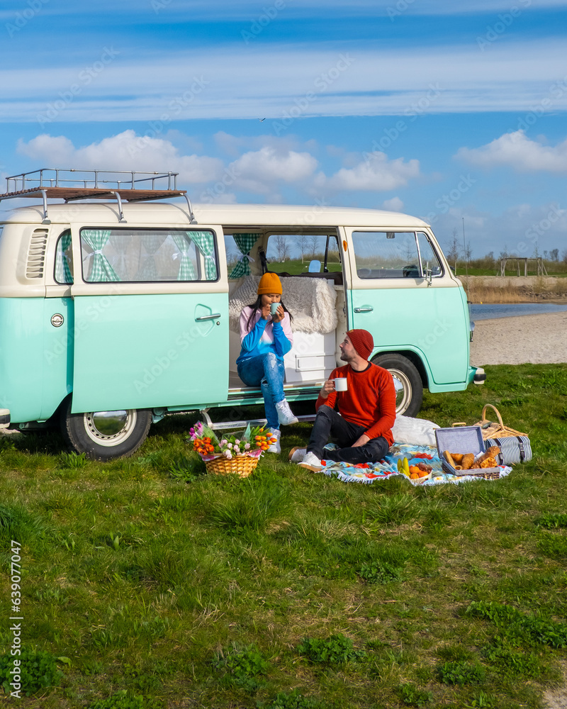 couple doing a road trip with an old vintage car in the Dutch flower bulb region with tulip fields during Spring in the Netherlands, camper van with picnic in front