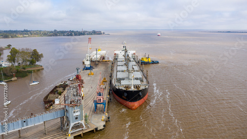 Self unloading bulk carrier arriving in South American port. Assisted by tug boat. Aerial front view.