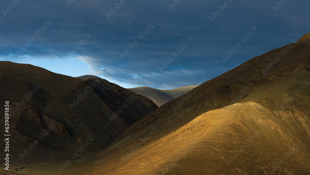 A dramatic view of silhouette of mountains with sunrays falling through clouds A dramatic view of silhouette of mountains with sunrays falling through clouds