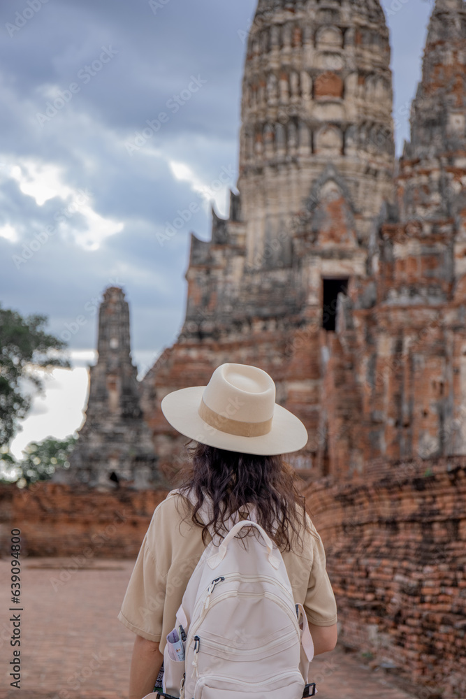 Backview of tourist girl in straw hat with rucksack admiring at ancient high tamples, exotic adventure, tourism as lifestyle concept, copy space