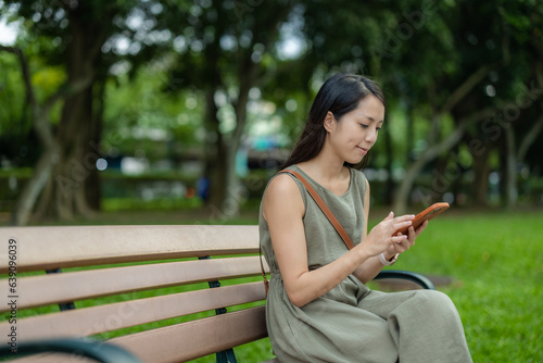 Woman use smart phone and sit at bench in the park