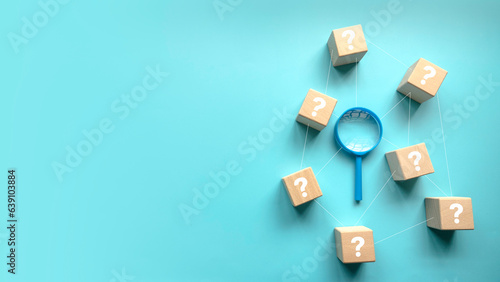 QnA or questions and answers concept. Blue magnifying glass with question symbol on wooden cube over a blue background with copy space .