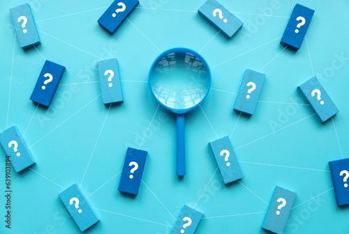 QnA or questions and answers concept. Blue magnifying glass with question symbol on wooden cube over a blue background.