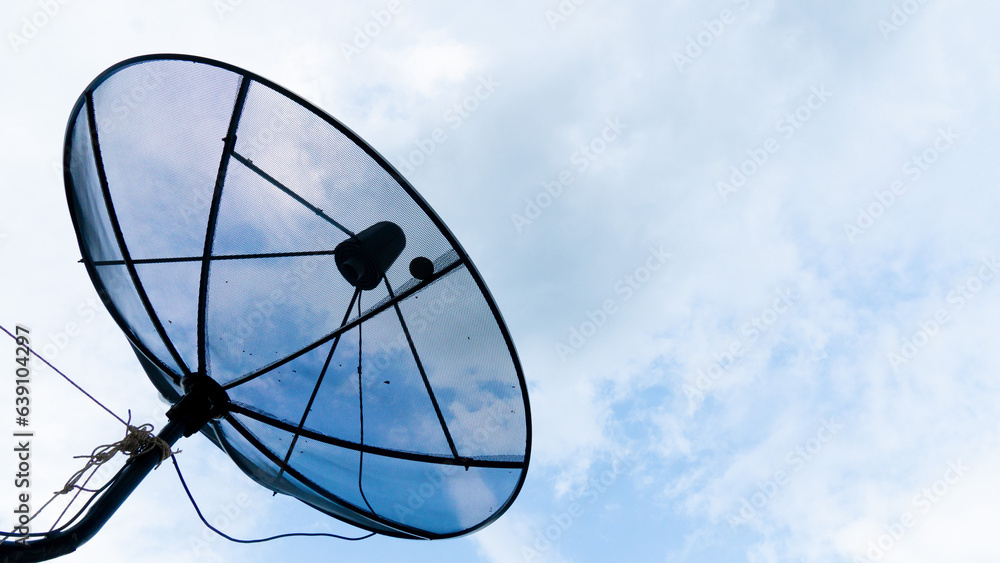 Abstract of black steel satellite dish that looks up into the sky. Background of blue sky and white clouds.