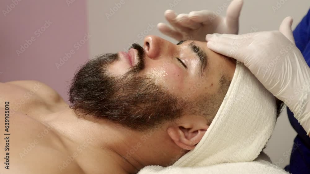 Handsome latin mexican guest receives facial skin care treatment at wellness center spa hotel moisture mask. gloves hands Handsome latin mexican guest receives facial skin care treatment at wellness center spa hotel moisture mask. gloves hands