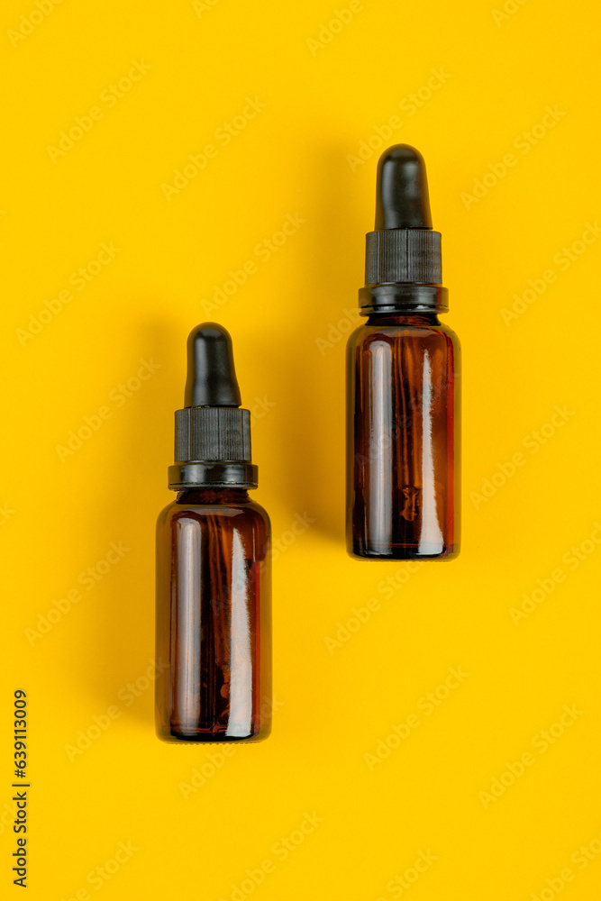 Cosmetic bottles made of dark amber glass on yellow background Cosmetic bottles made of dark amber glass on yellow background