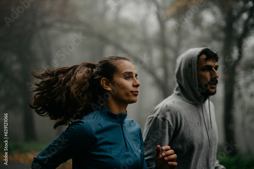 Two joggers immersed in the quiet beauty of the foggy forest during the early hours of the day.