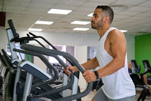 Strong Hispanic man doing elliptical training at a gym.