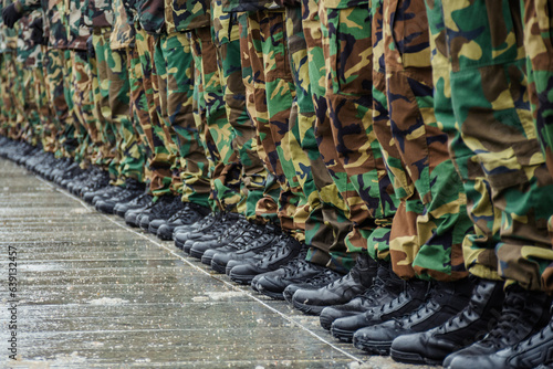 A close-up view of a row of soldiers standing in formation on a wet pavement, wearing black combat boots and camouflage military uniforms