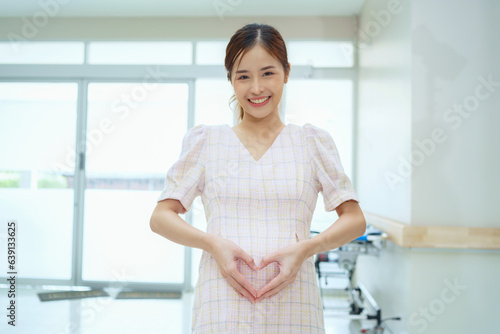 Happy and excited pregnant woman making heart shape on her belly at hospital