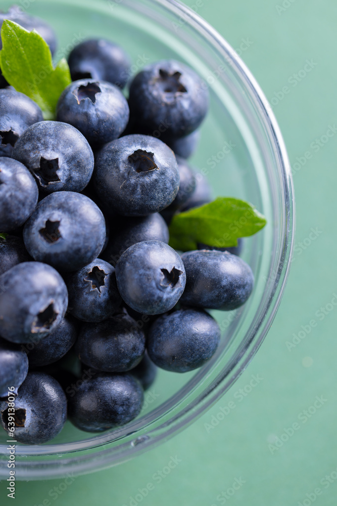 Micro close up of blueberries in glass bowl with copy space on green background Micro close up of blueberries in glass bowl with copy space on green background