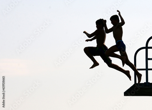 silhouettes of two teenagers jumping together from diving tower to waters of Lake Geneva, Paquis beach, Geneva, Switzerland, Europe 