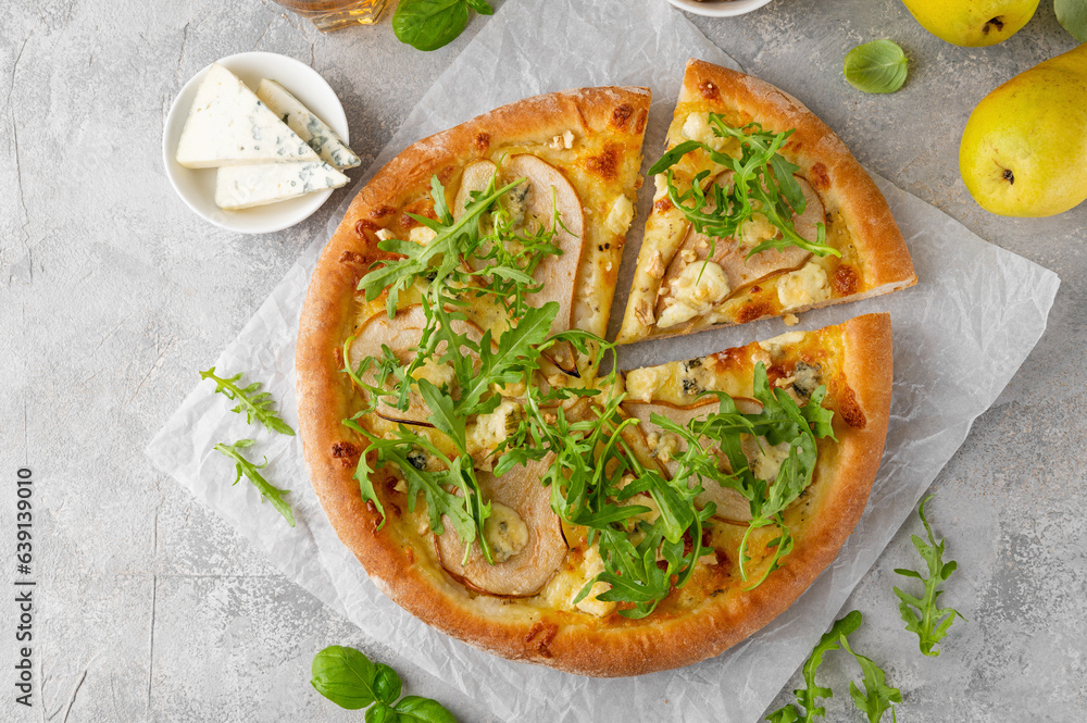 Delicious pizza with pears, gorgonzola cheese, walnuts and arugula on a gray concrete background.