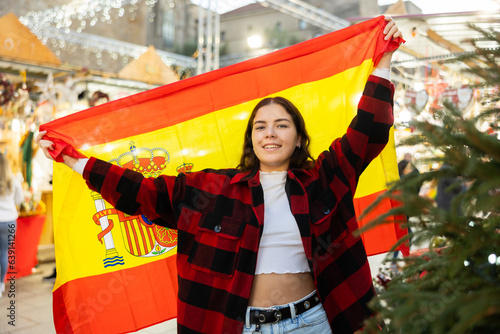 Happy girl waving Spain flag at street new year fair