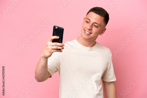 Young Brazilian man isolated on pink background making a selfie © luismolinero