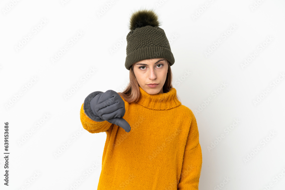 Young girl with winter hat isolated on white background showing thumb down with negative expression