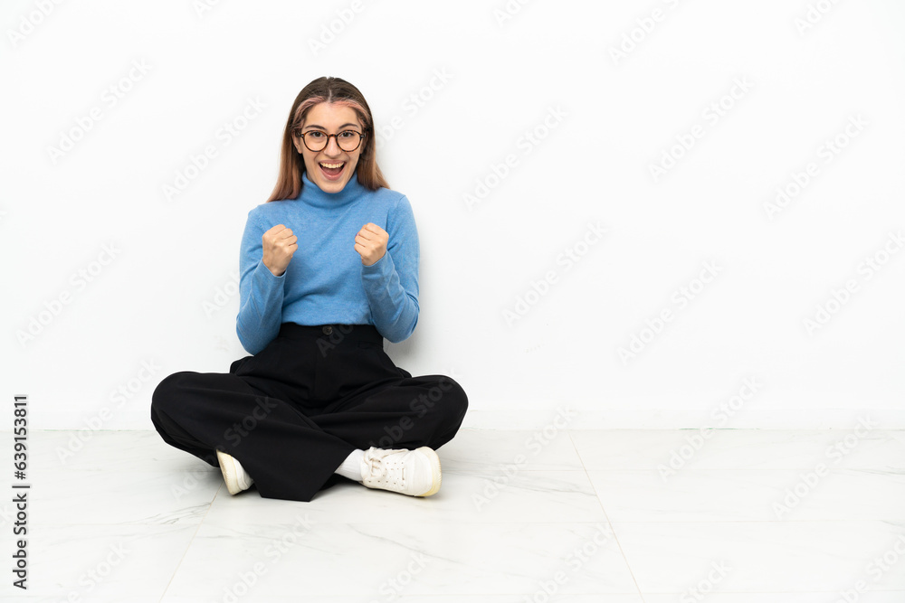 Young Caucasian woman sitting on the floor celebrating a victory in winner position Young Caucasian woman sitting on the floor celebrating a victory in winner position