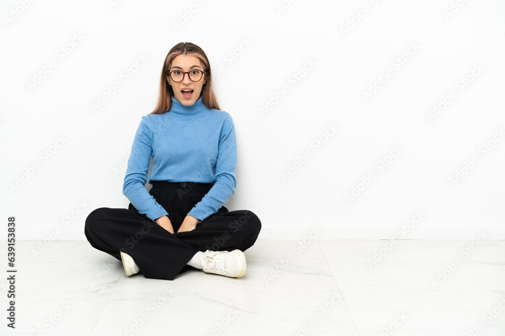 Young Caucasian woman sitting on the floor with surprise facial expression Young Caucasian woman sitting on the floor with surprise facial expression