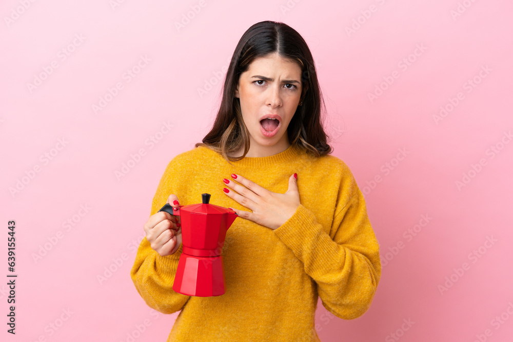 Young Italian woman holding a coffee maker isolated on pink background surprised and shocked while looking right Young Italian woman holding a coffee maker isolated on pink background surprised and shocked while looking right