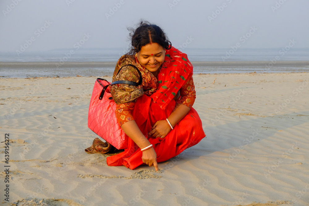 South asian middle aged hindu woman writing something on a beach with her finger, Lady in traditional dress 