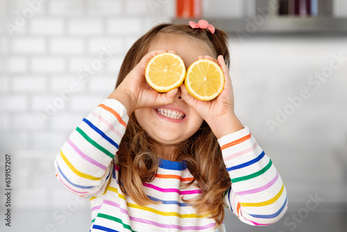 Happy little girl holding lemons against her eyes
